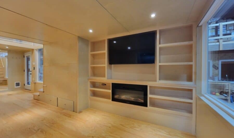 Interior view of a modern tiny house with built-in shelves and a fireplace.
