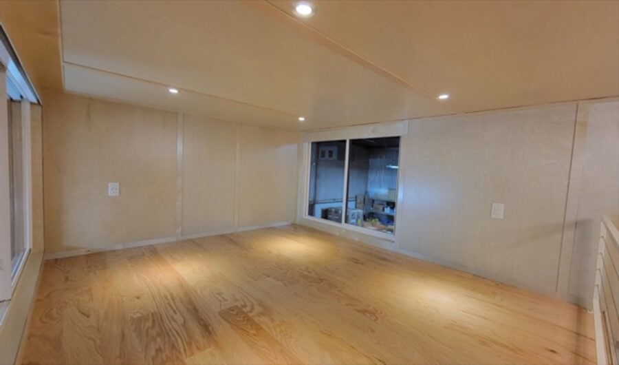 Spacious tiny house interior with wooden floors and large windows.
