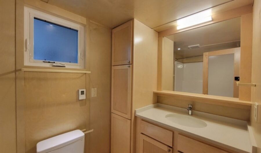 Tiny house interior featuring a compact bathroom with wooden cabinetry and a small window for natura.