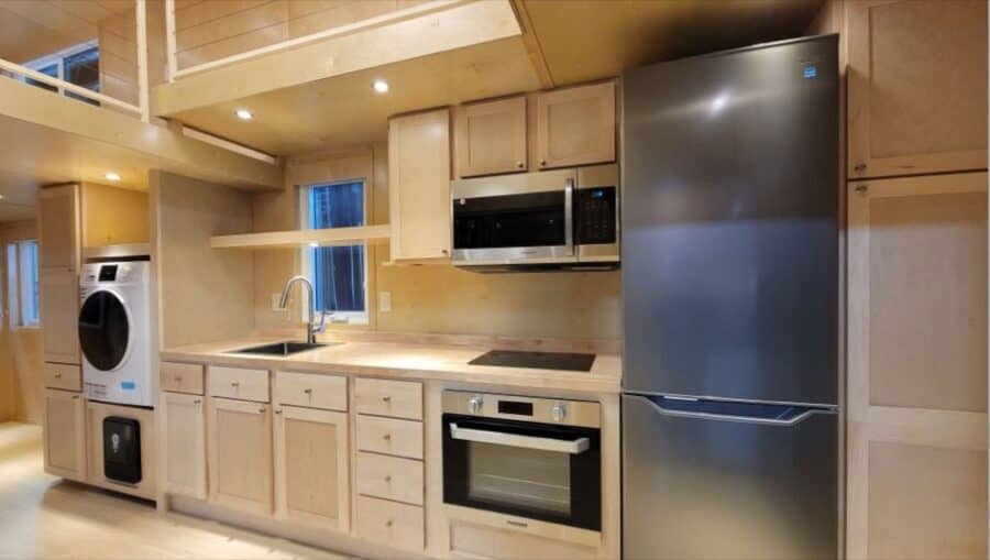 Compact, modern tiny house kitchen with appliances and storage.