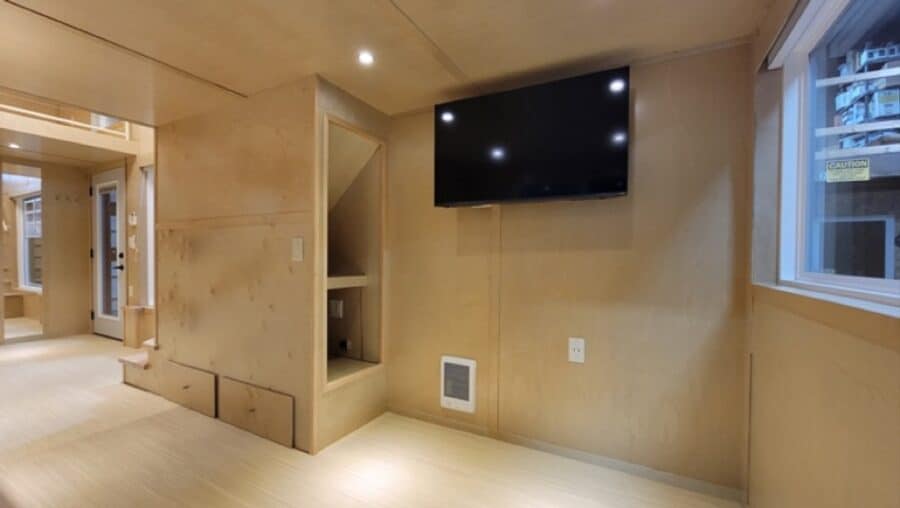 Modern tiny house interior with wall-mounted TV and cozy built-in shelving.