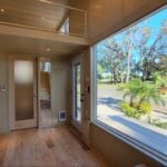 Modern tiny house interior featuring oak floors and expansive window views of lush greenery.