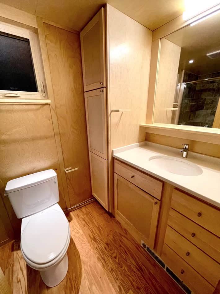 Compact tiny house bathroom with wooden cabinets and a small sink.