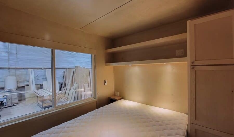 Cozy tiny house bedroom with large window and built-in storage.
