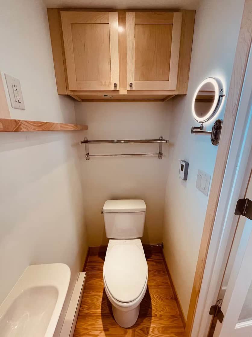 Compact tiny house bathroom with wooden cabinets and modern fixtures.