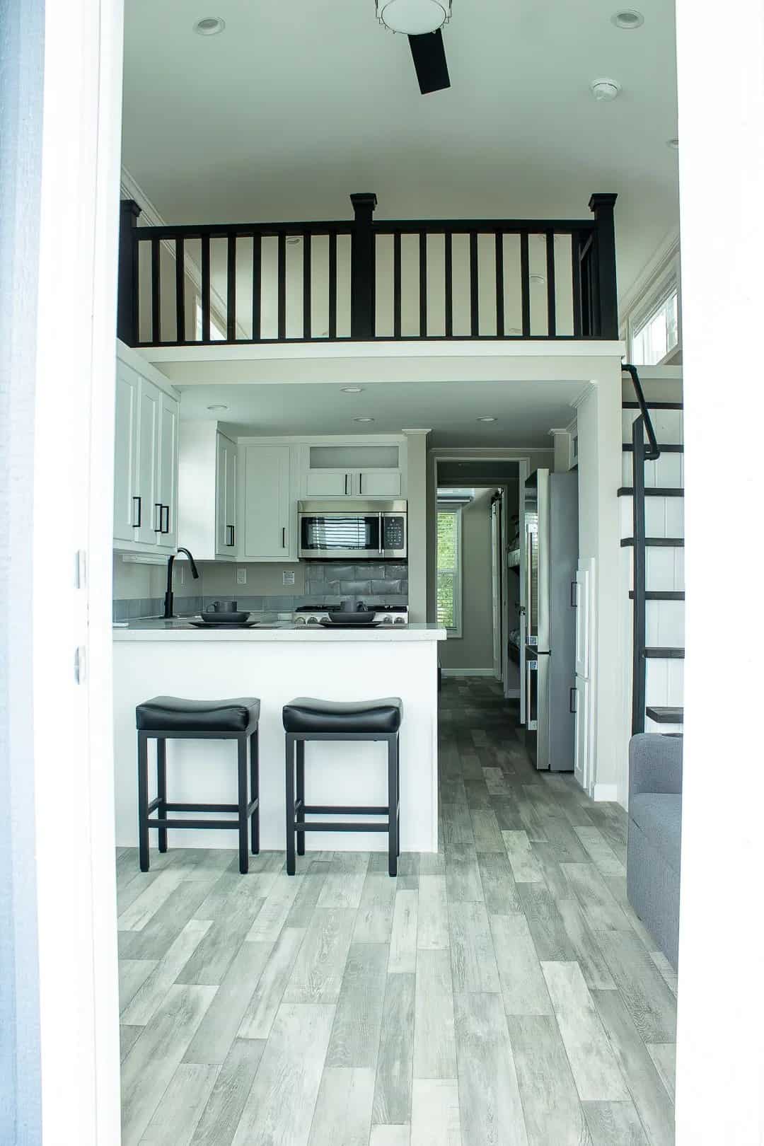Kitchen with white shaker cabinets and a breakfast bar beneath the loft railing, with stairs at right