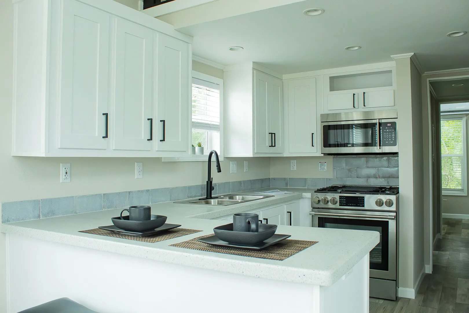 White shaker kitchen with stainless range, microwave, and sink, with place settings on the counter