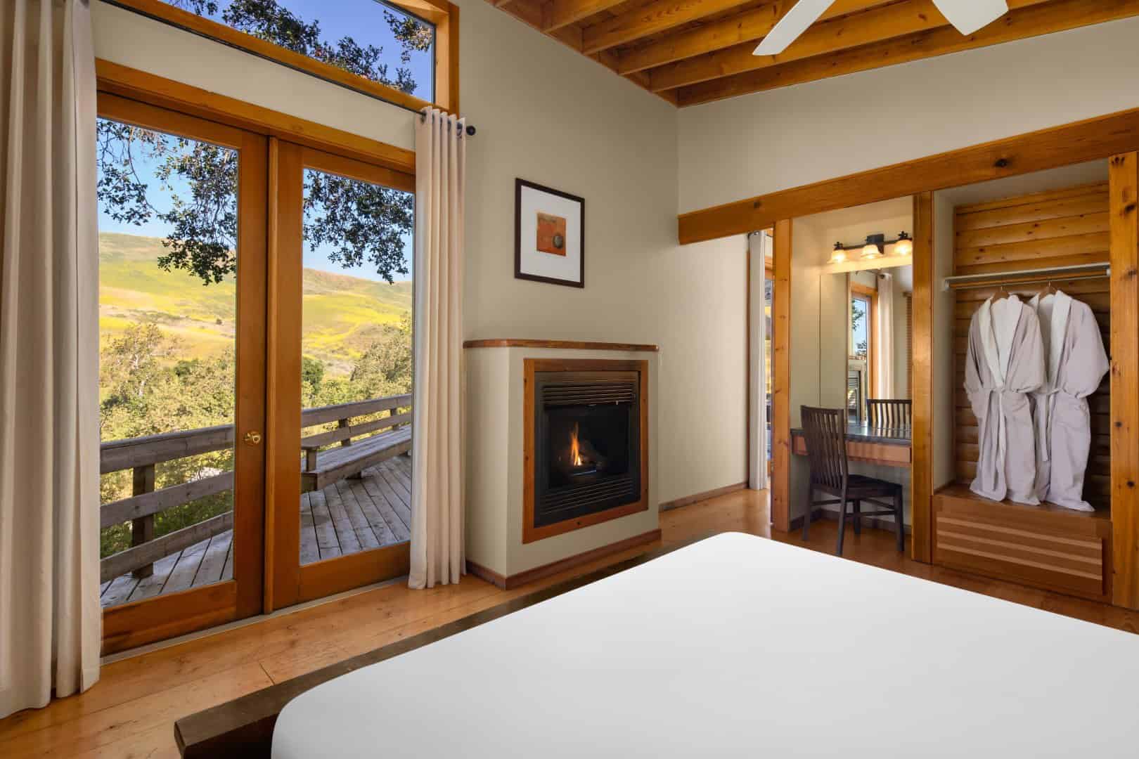 Bedroom with glass doors to a deck, hills beyond, and a fireplace