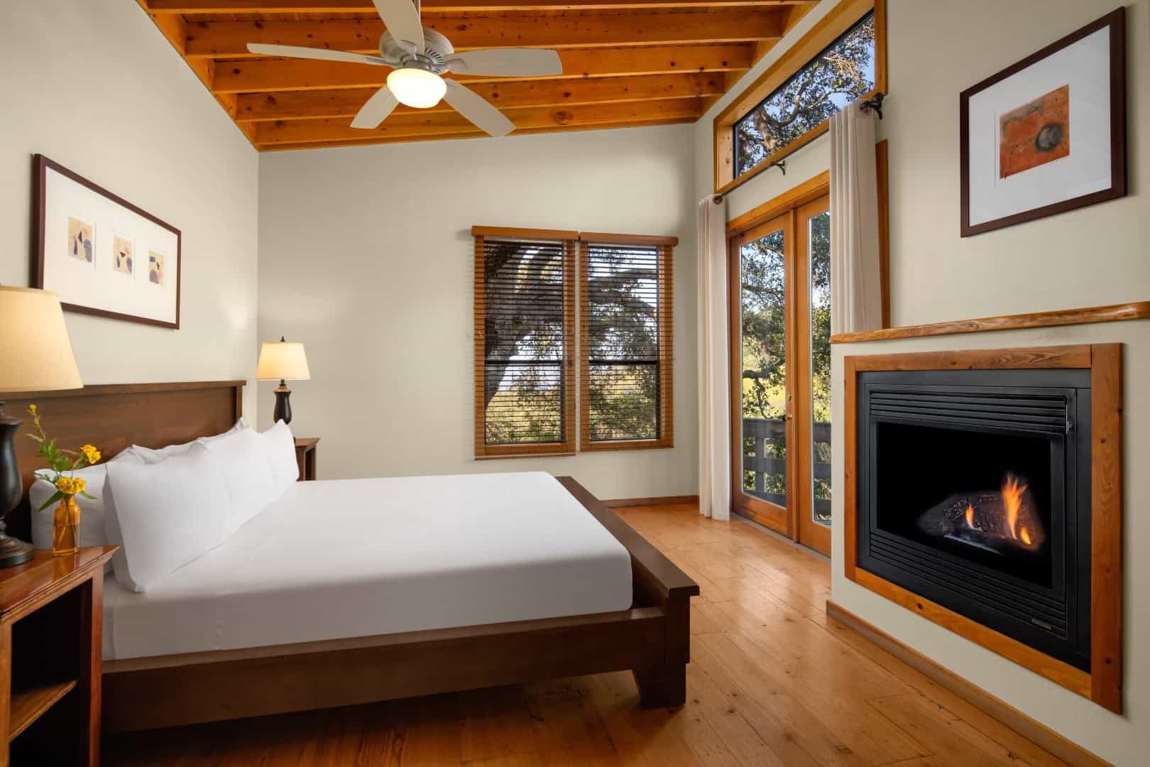 Bedroom with a bed, glass doors onto trees, and a fireplace