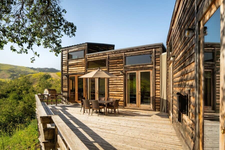 Log cabin and a wood deck with a table, chairs, and a grill, looking over hills