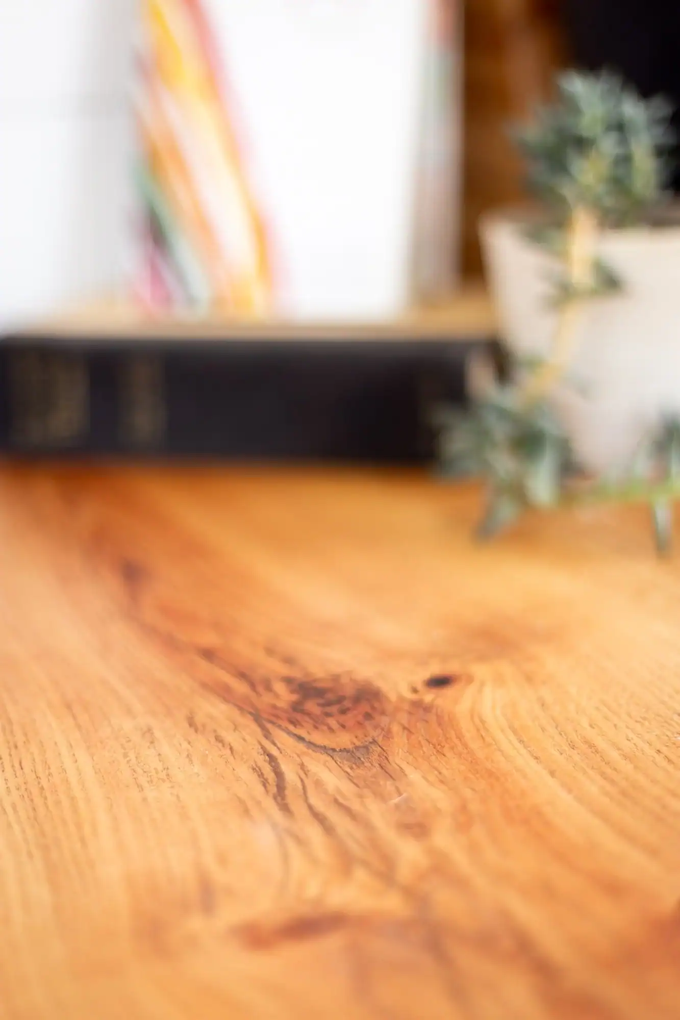 Close-up of a wooden table with a blurred background of a tiny house interior and potted plants.