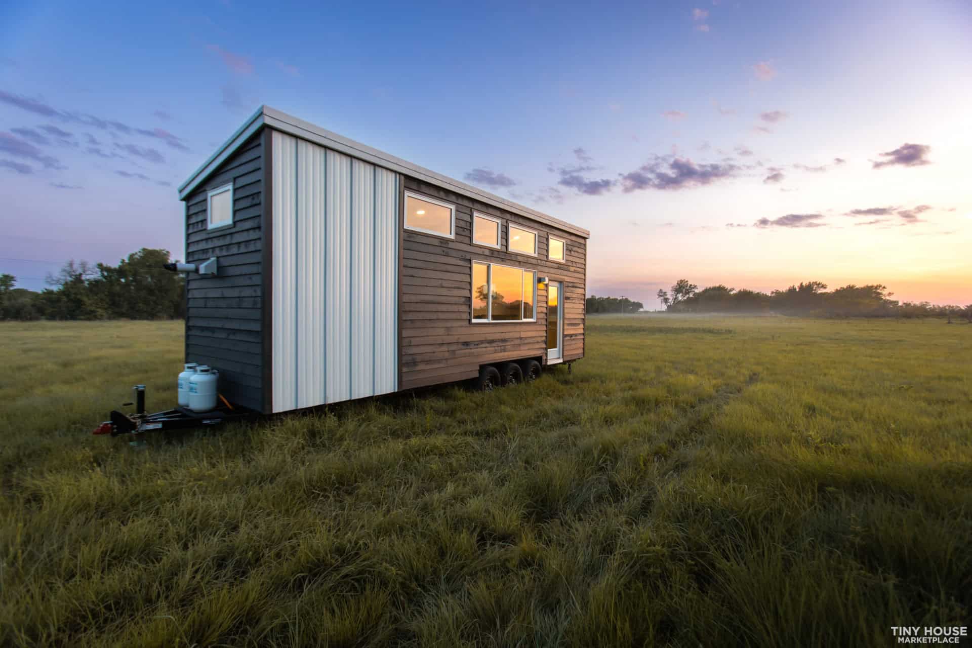 Tiny house on wheels with modern design in a grassy field during sunset.