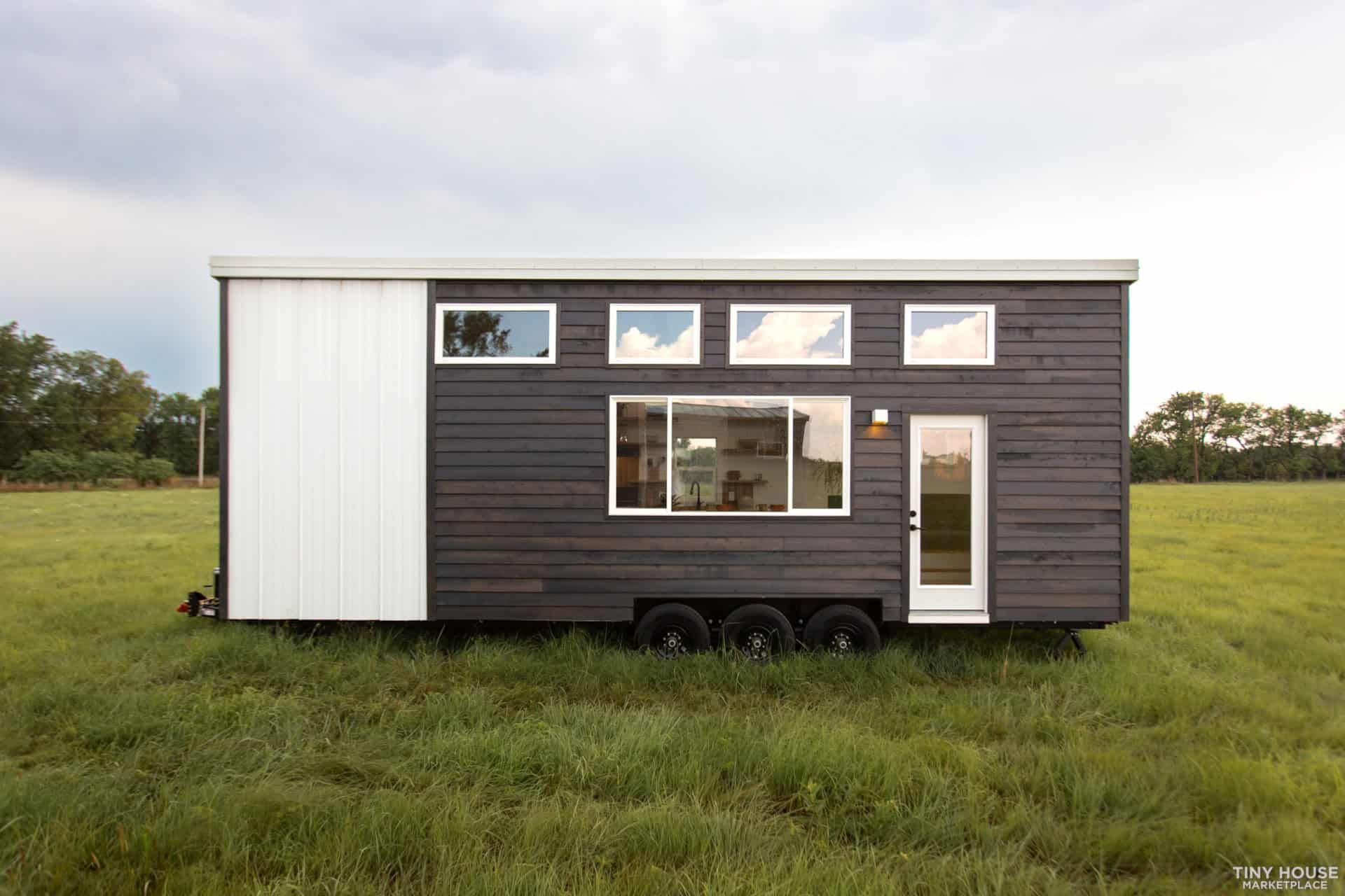 Tiny house on wheels with modern black and white exterior in a grassy field.