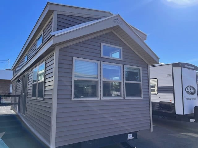 Gray Elevation Woodland Loft park model on the Wilder RV lot, showing the tall loft gable and a bank of side windows