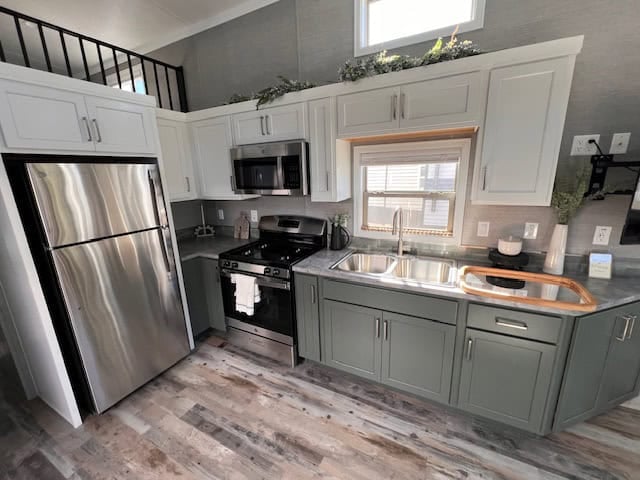 Full-size stainless refrigerator beside the green-cabinet kitchen, with the loft railing above