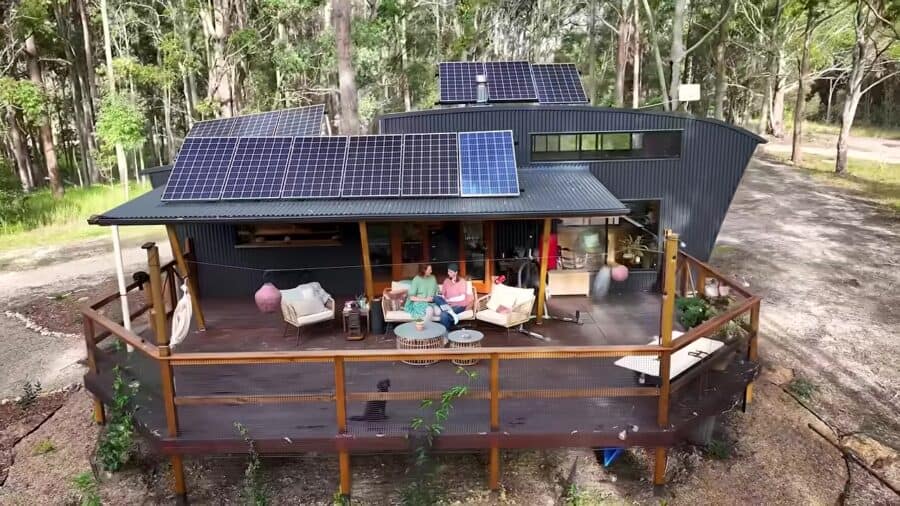Dark corrugated curved tiny house with a large covered timber deck, solar on the roof, and outdoor lounge in New South Wales bush