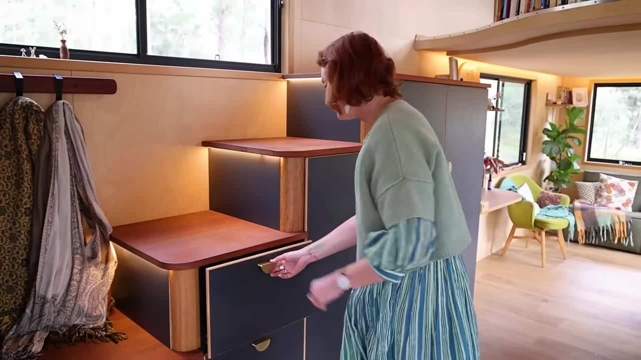 Charcoal storage stair with rounded timber treads and LED strips, a deep drawer pulled open, lounge and curved loft behind