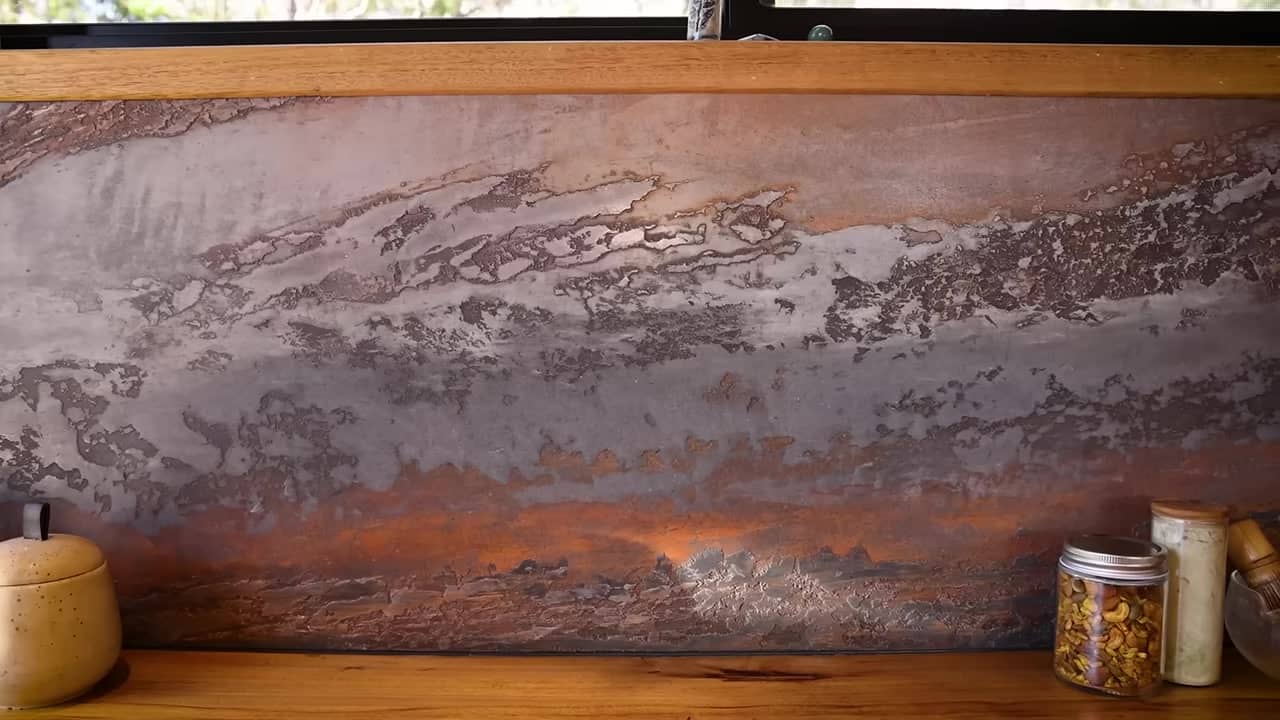 Close-up of a layered Venetian plaster splashback in charcoal, rust, and copper over a live-edge timber kitchen bench