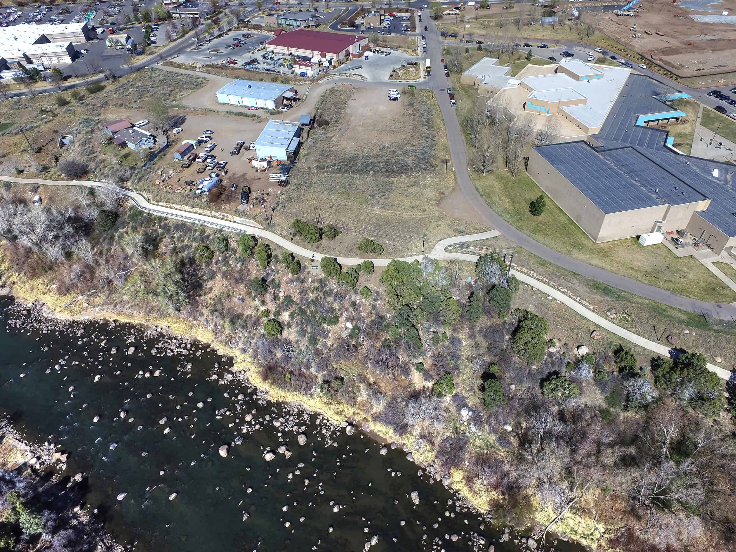 Aerial of the Animas River, a rocky bank, and a paved trail — site context for Escalante Village in Durango, not the tiny-home pads