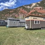 Three tiny houses on wheels on grass with red-rock cliffs behind them at Escalante Village in Durango, Colorado