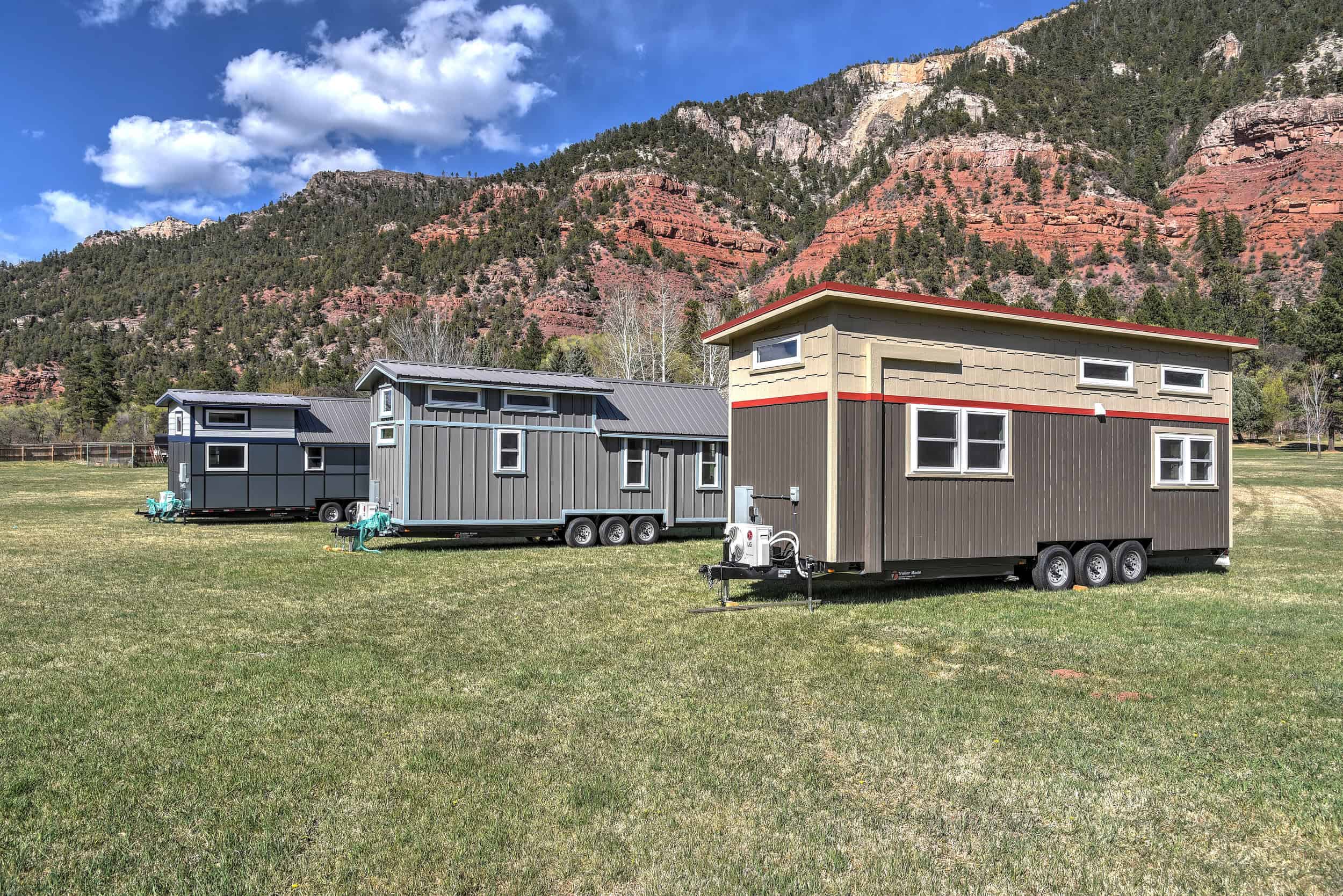 Three tiny houses on wheels on grass with red-rock cliffs behind them at Escalante Village in Durango, Colorado