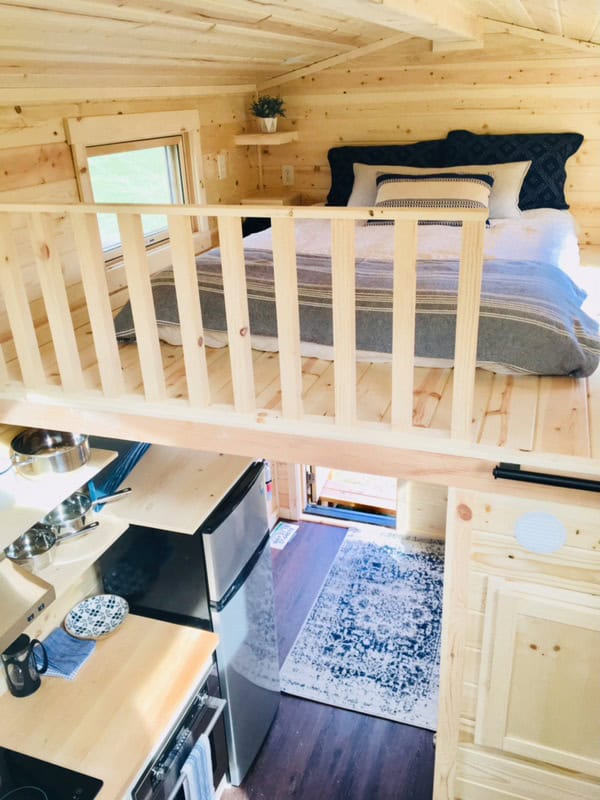 Looking down from a loft to a compact kitchen and entry in a light-wood tiny house at Escalante Village in Durango