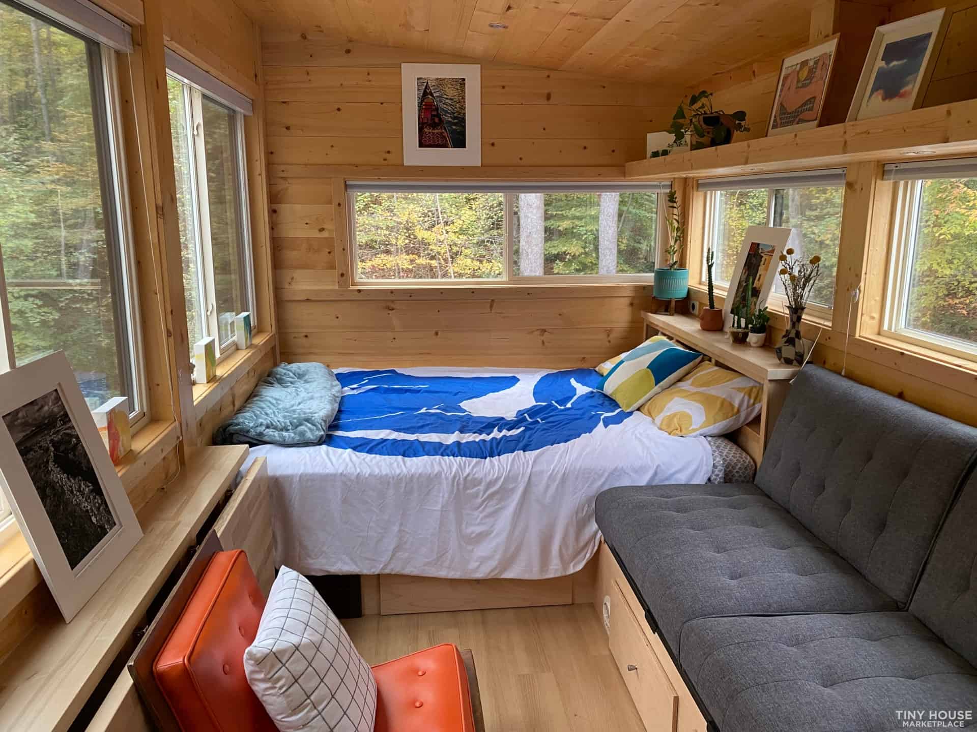 Built-in bed under windows beside a gray fold-flat couch with storage drawers below