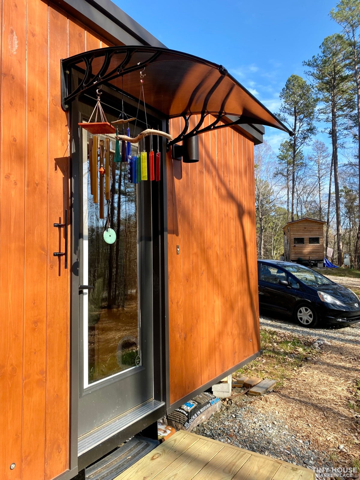 Full-light glass entry door with a curved awning on the stained siding of the tiny house