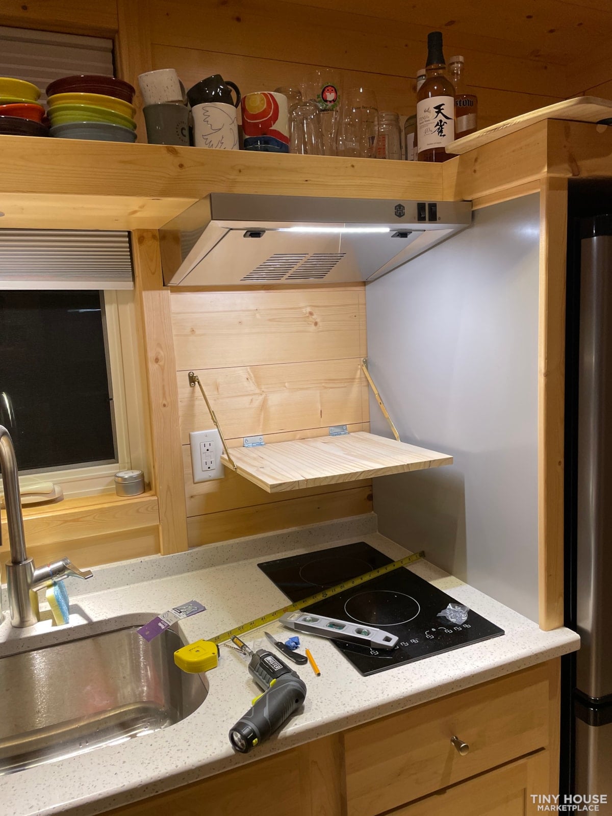 Hinged wooden panel under the range hood folded down to form a shelf above the induction cooktop