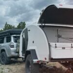 White Escapod TOPO2 Nomad with galley open on rocky terrain, a Toyota 4Runner visible in frame