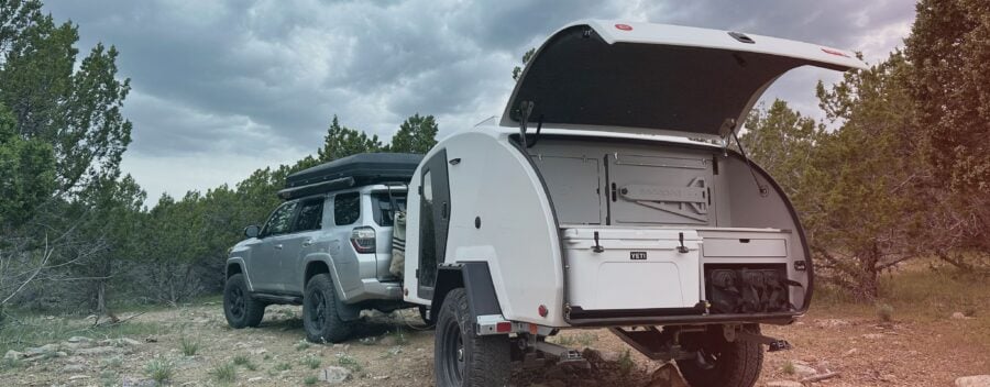 White Escapod TOPO2 Nomad with galley open on rocky terrain, a Toyota 4Runner visible in frame