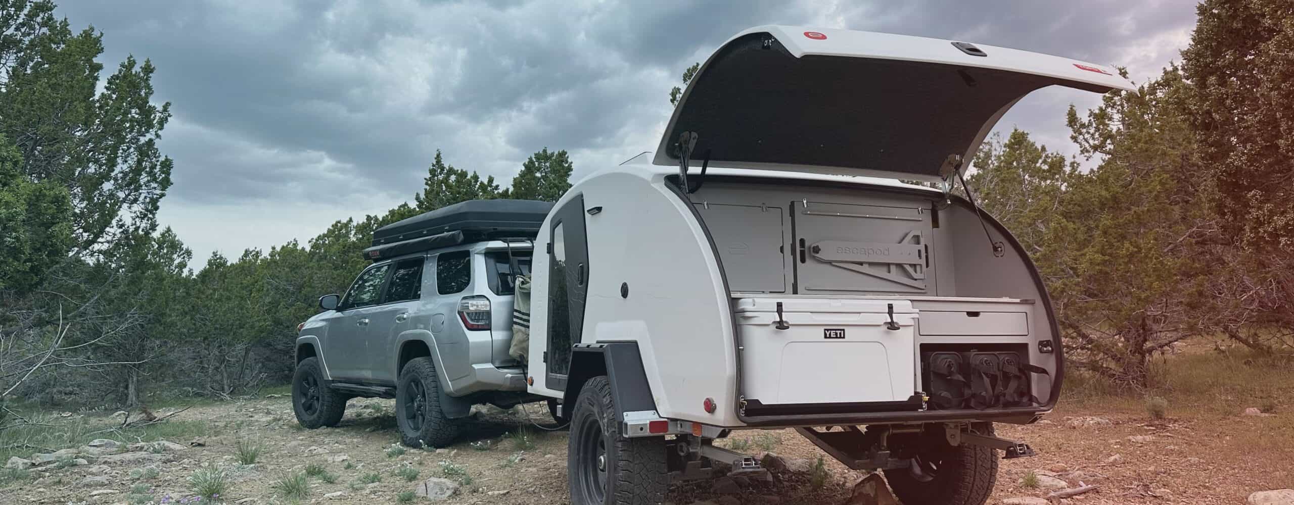 White Escapod TOPO2 Nomad with galley open on rocky terrain, a Toyota 4Runner visible in frame