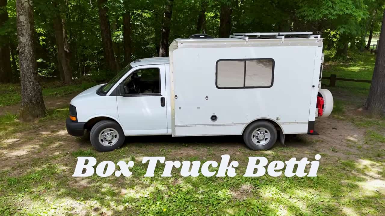 White Box Truck Betti tiny home parked in the woods with rooftop solar panels and spare tire