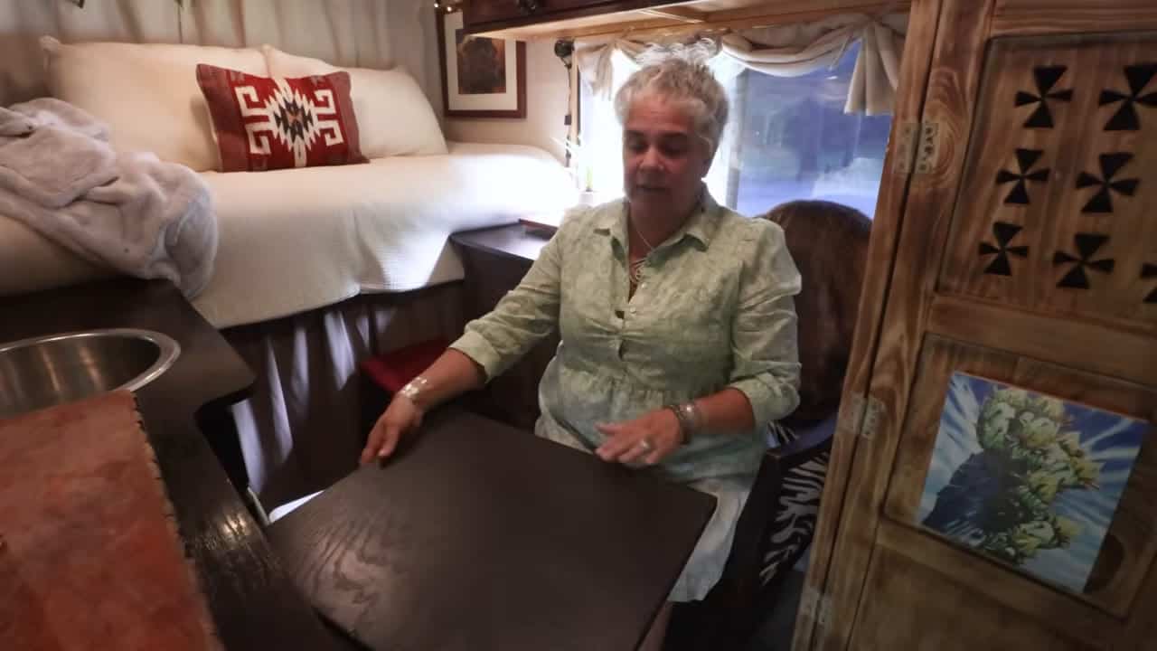 Eva demonstrating a pull-out hideaway wood table with the white bed and red accent pillow behind her