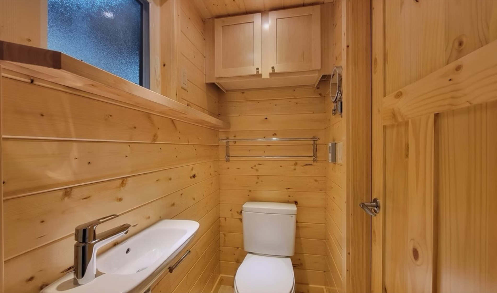 Bathroom with toilet, sink, and wood paneling in the eVista King Limited tiny house