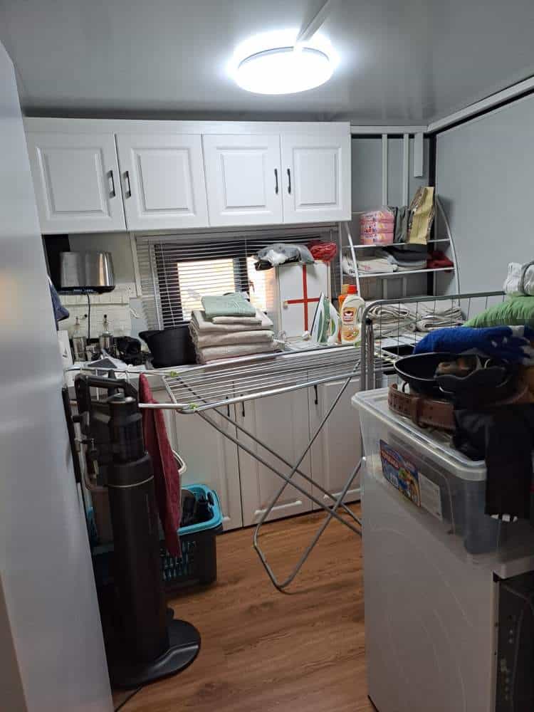 Separate utility room in the expandable prefab home in Cyprus with white cabinets, a sink, shelving, a drying rack and laundry equipment