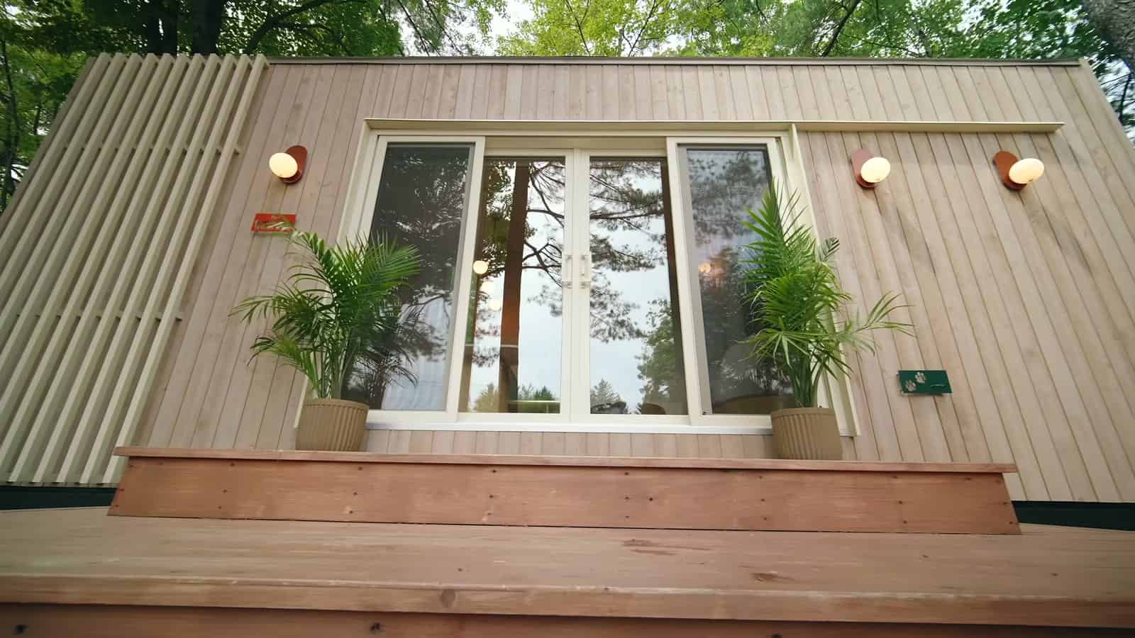 Entry wall of the B.Drop.24f with a wide window, two wall sconces, potted palms and a cedar deck beside a slatted privacy screen