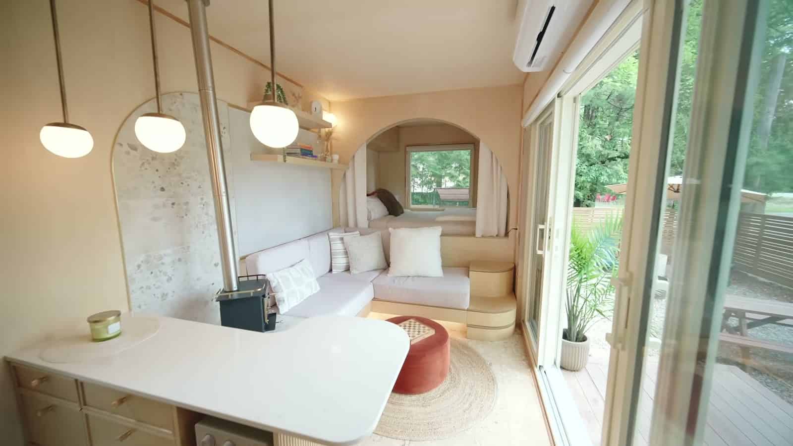 Interior of the B.Drop.24f looking toward the bed, three globe pendants, curved quartz counter, L-shaped sofa, red ottoman and glass doors to the deck