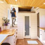 Kitchen and living in a 26-foot Tantalus tiny house, white shiplap, wood counters, stairs to the loft, range and tall black fridge