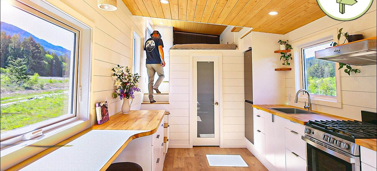 Kitchen and living in a 26-foot Tantalus tiny house, white shiplap, wood counters, stairs to the loft, range and tall black fridge