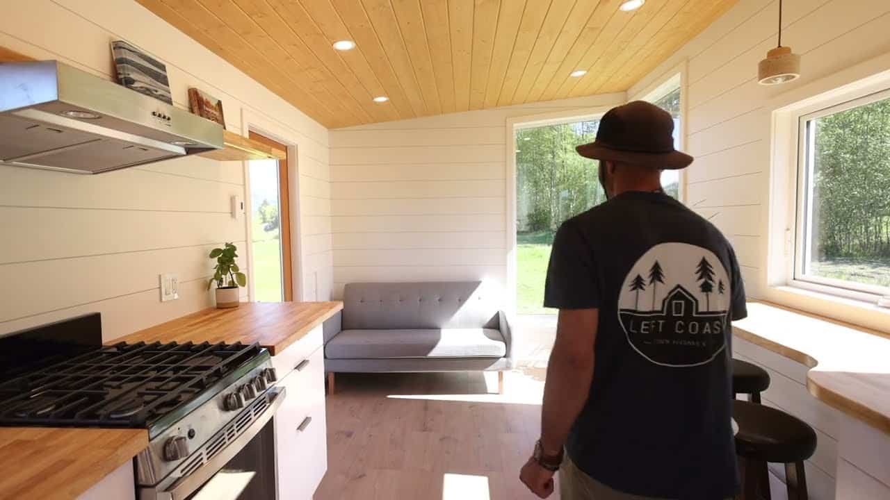 Living end of the Tantalus: grey sofa, dining counter with two stools, large window to the trees, kitchen range at left