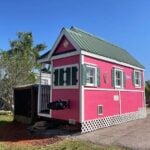 Charming pink tiny house with a green metal roof, perfect for small space living and vacation rental.