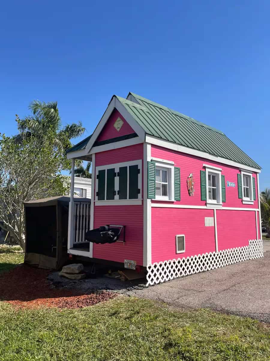 Charming pink tiny house with a green metal roof, perfect for small space living and vacation rental.