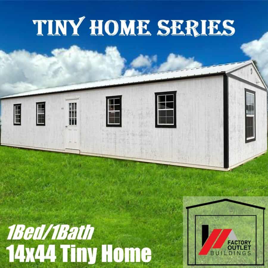 White 14x44 tiny home with black trim and a white metal roof on grass under a blue sky