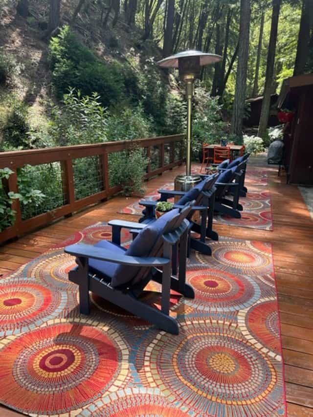 Redwood deck with blue Adirondack chairs, a patterned outdoor rug, and a patio heater