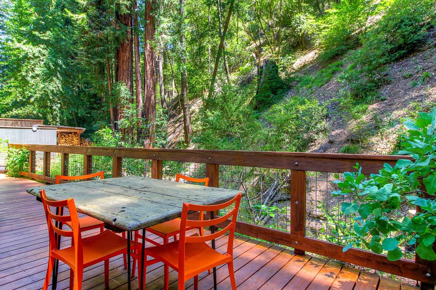 Redwood deck with an outdoor dining table and orange chairs surrounded by forest