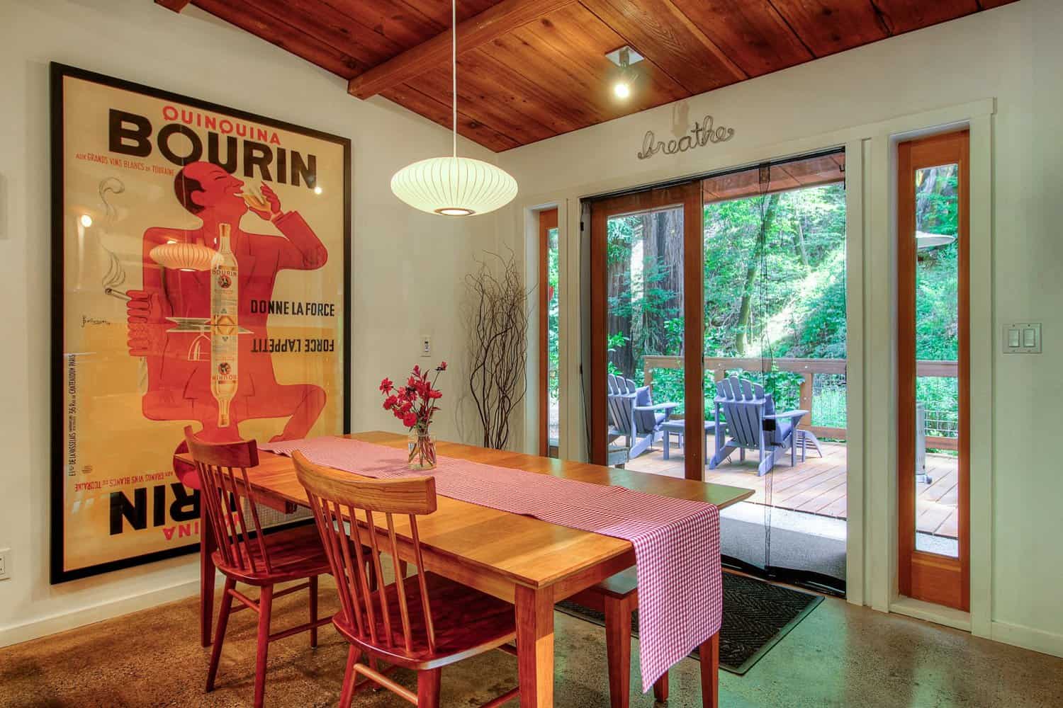 Dining table with red chairs beside glass doors and a large vintage poster