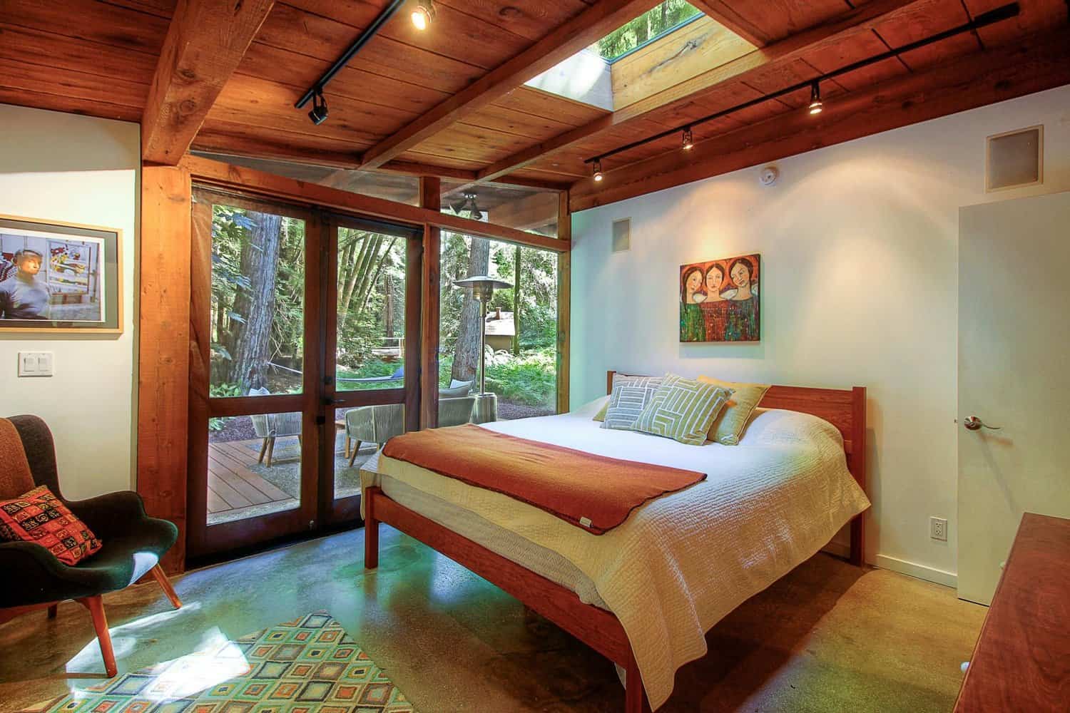 Main bedroom with California king bed, wood ceiling, skylight, and glass doors to the forest
