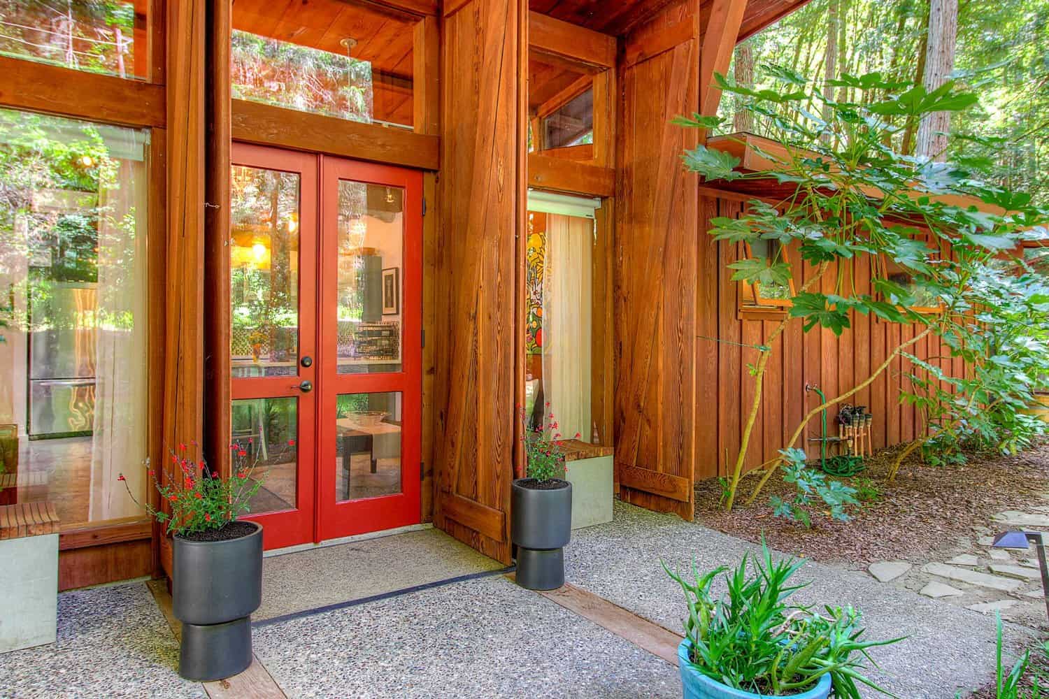 Red glass double front doors set in redwood siding, with potted plants