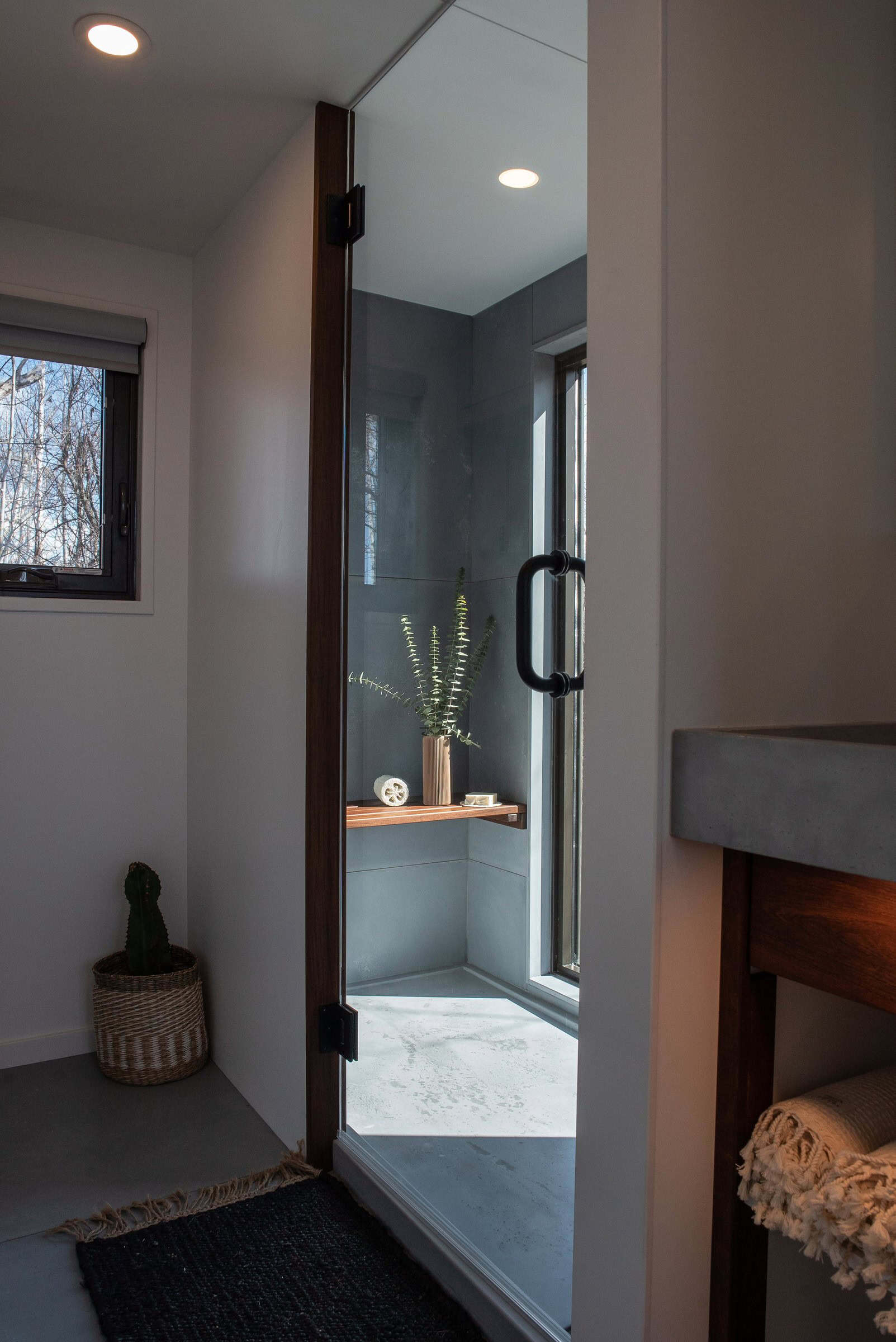 Halcyon 01 bathroom: glass walk-in shower with grey tile and a wood bench, concrete-style vanity edge, white towels — soaker tub is printed as standard, walk-in as an option